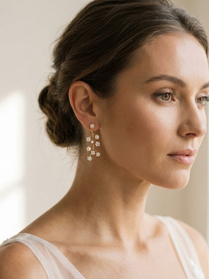 Close-up of delicate TALIA earrings on a bridal model with soft updo, ivory background, highlighting faux pearls and ivory beads.